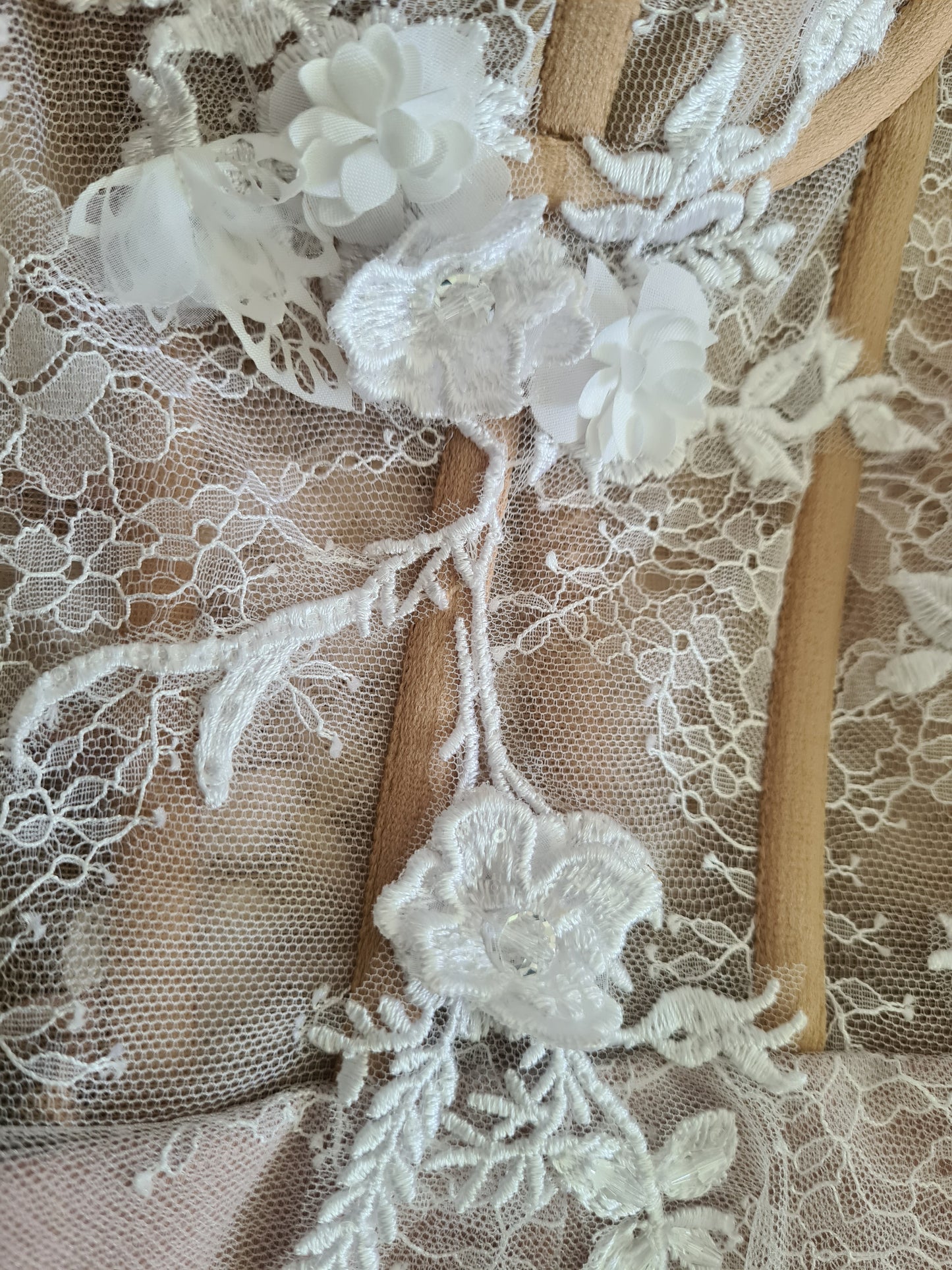 Beautiful wedding dress with a sheer cupped bustier, delicate ivory lace overlay and 3D floral lace hand applique detail. The dress has a nude colour satin lining, overlaid with delicate lace and a layer of soft flowing tulle. The dress has a lace up ribbon corset back and concealed zipper in the skirt. Lace close up